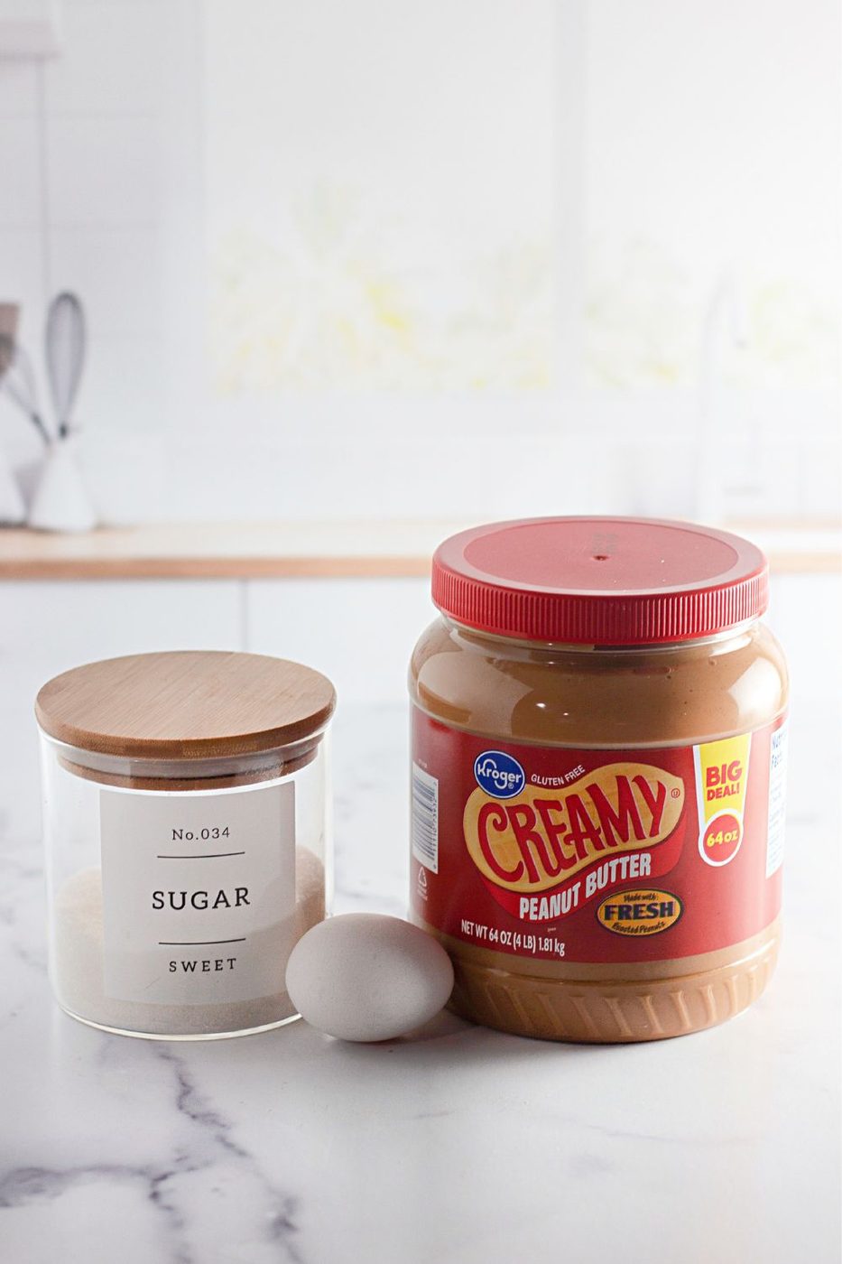 jar of granulated sugar, one egg and tub of peanut butter sitting on marble counter