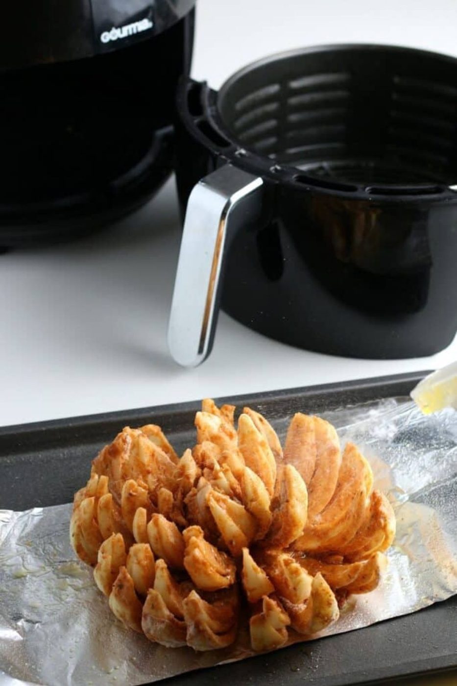 air fryer basket with a Air Fryer Blooming Onion on a tray in front on a plate