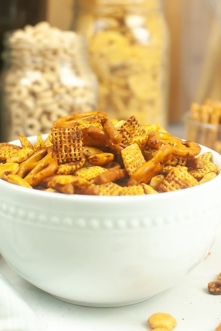 chex mix in a bowl with jars of the items mixed in it behind it 