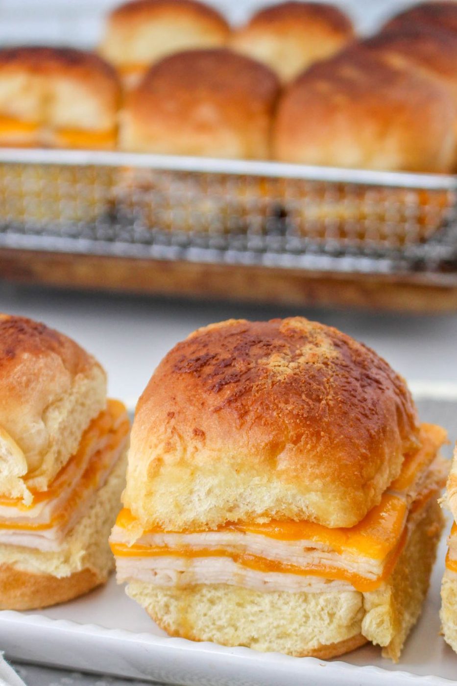 sliders on a tray with more sliders in a baking tray behind it on table 