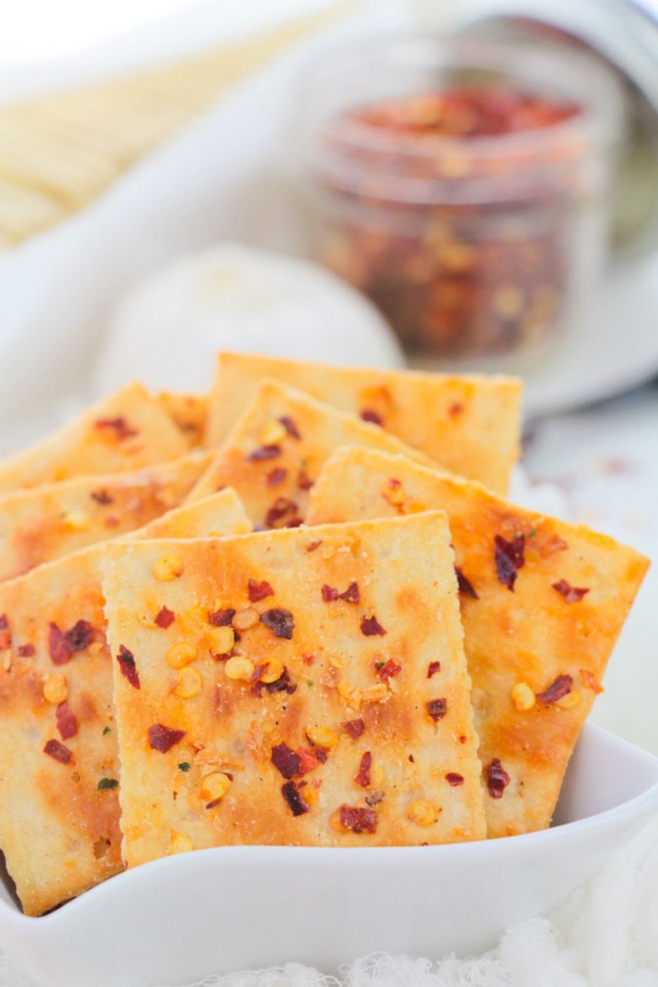 a bowl of spicy crackers on table with a jar to side full of red pepper flakes 