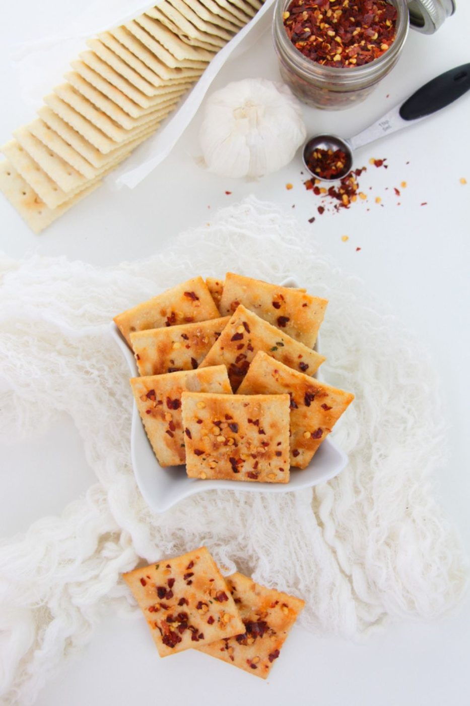 Alabama fire saltine crackers in a bowl on table with a saltine packet behind it and peppers in a measuring spoon to side 