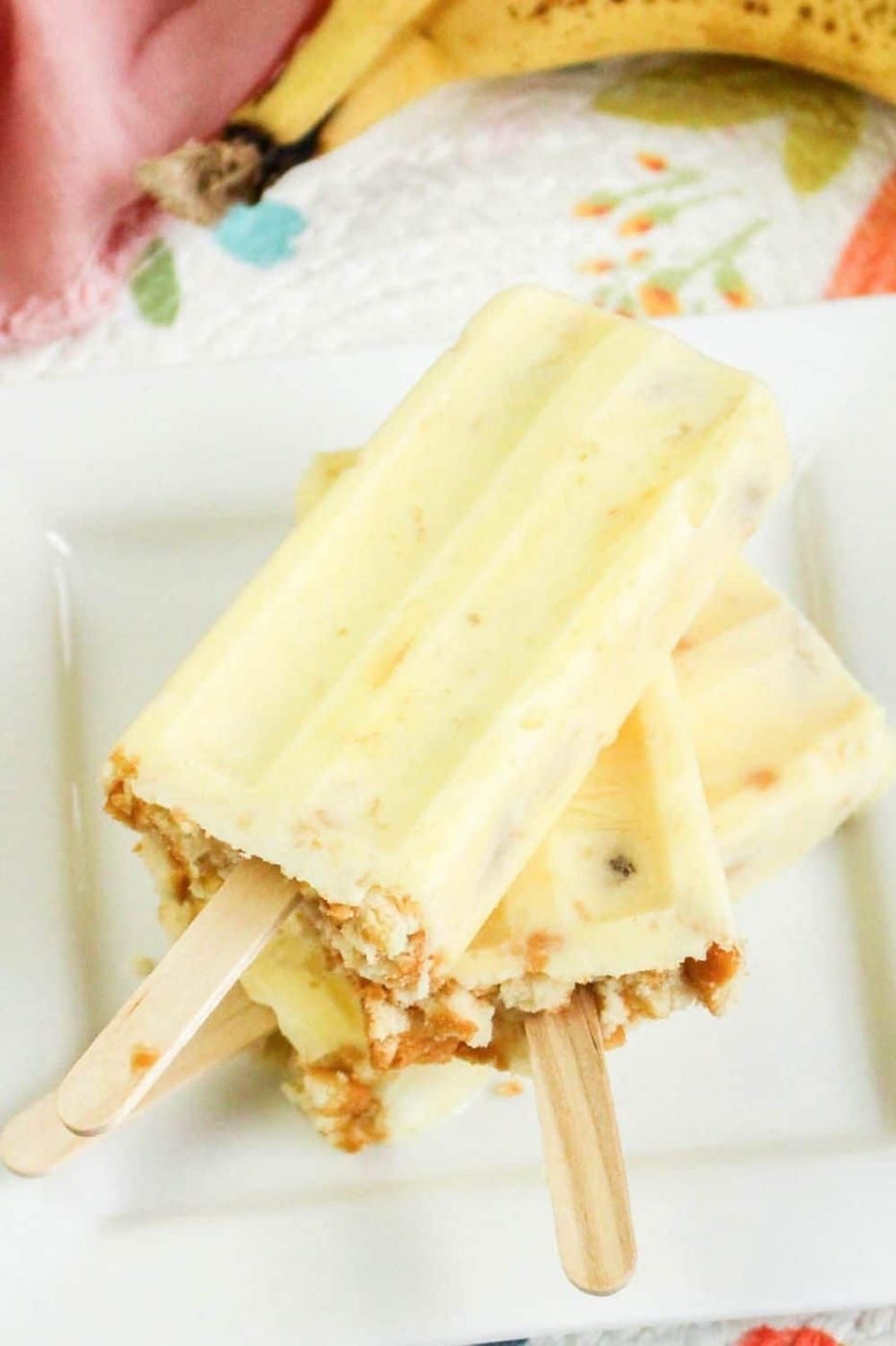 banana cream pie popsicles stacked on a plate with browned bananas behind it 