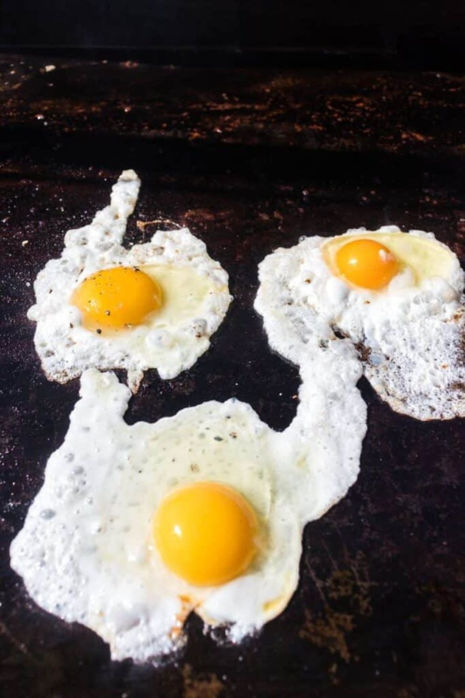 three eggs being cooked on a blackstone griddle 