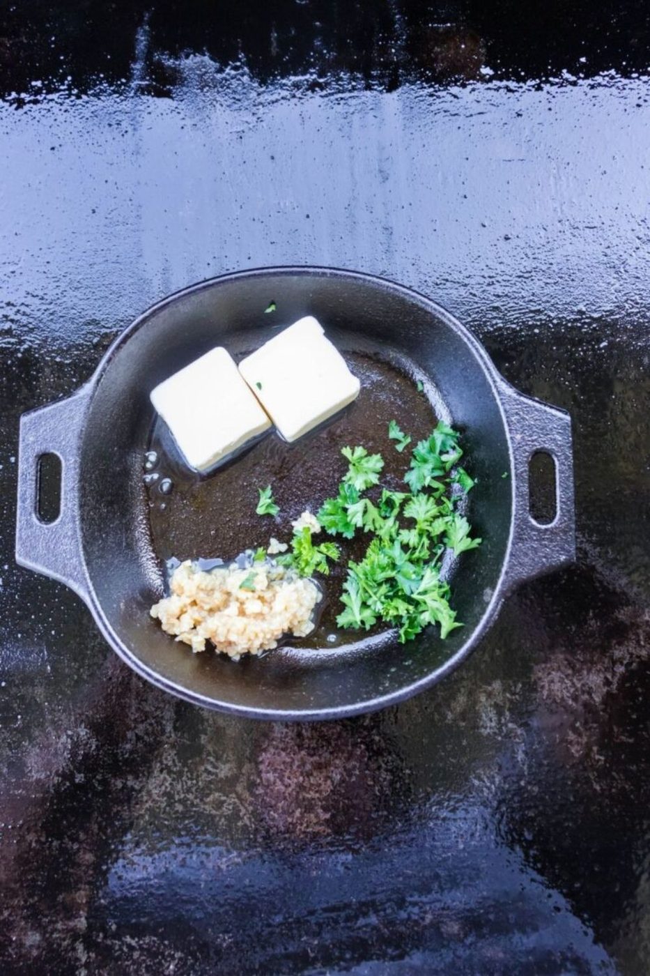 cast iron skillet on a blackstone grill with butter, garlic and herbs in pan