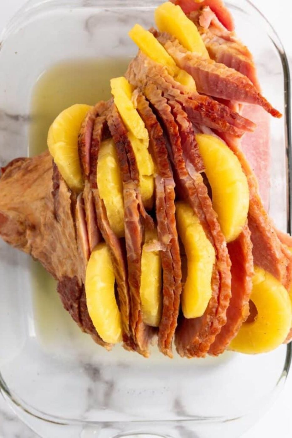 casserole dish with ham and pineapples in between slices of ham