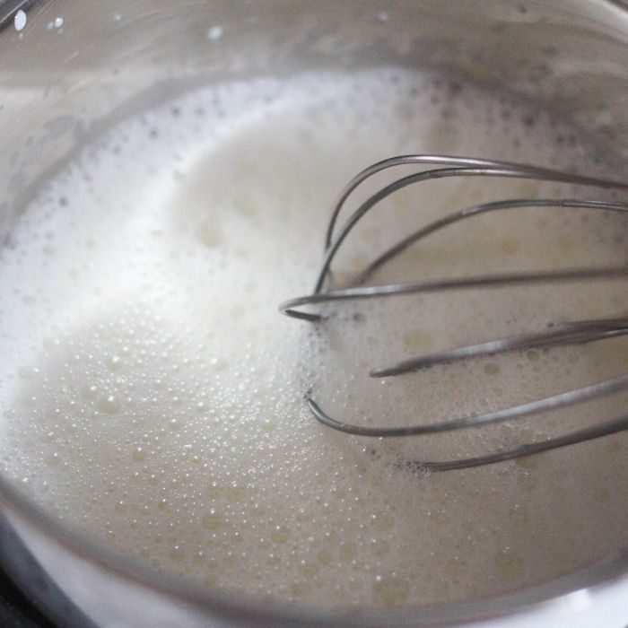 frothing milk in saucepan with a whisk