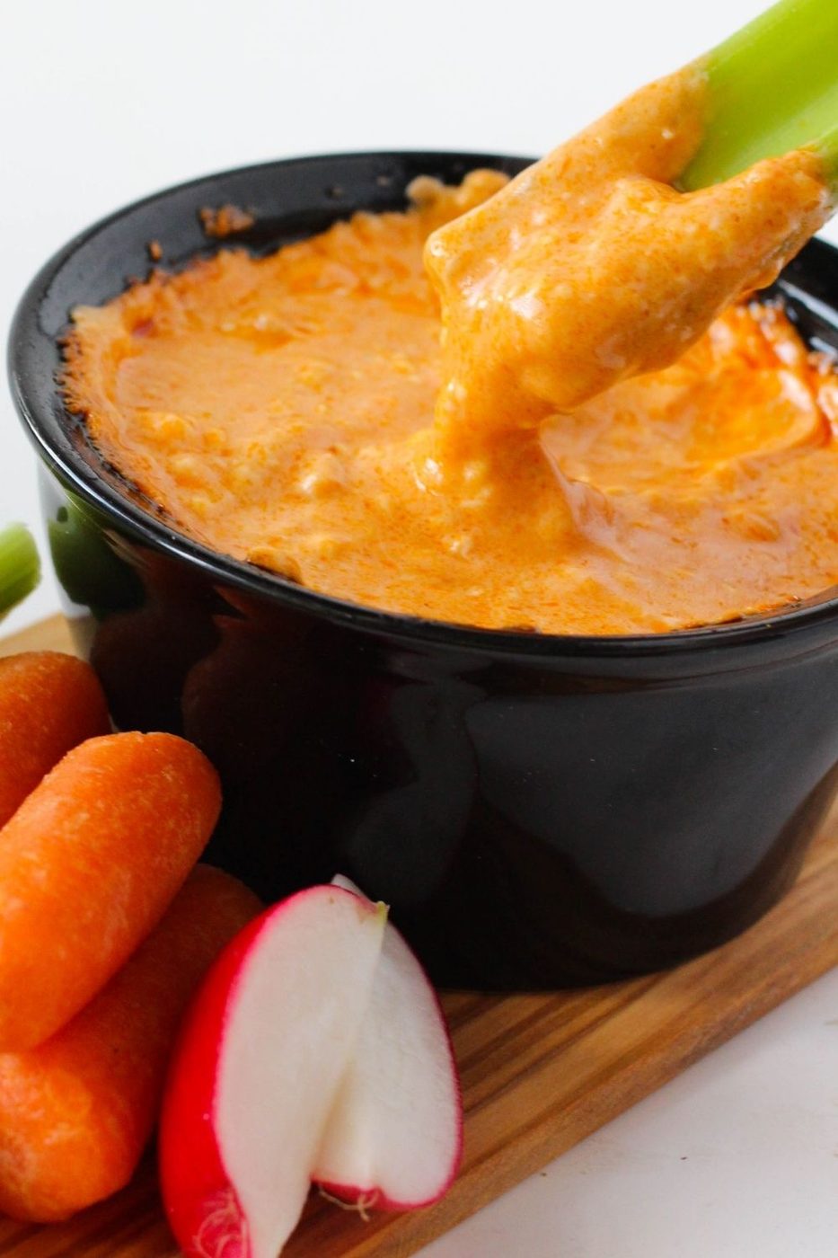 celery stick pulling up out of a bowl of buffalo dip