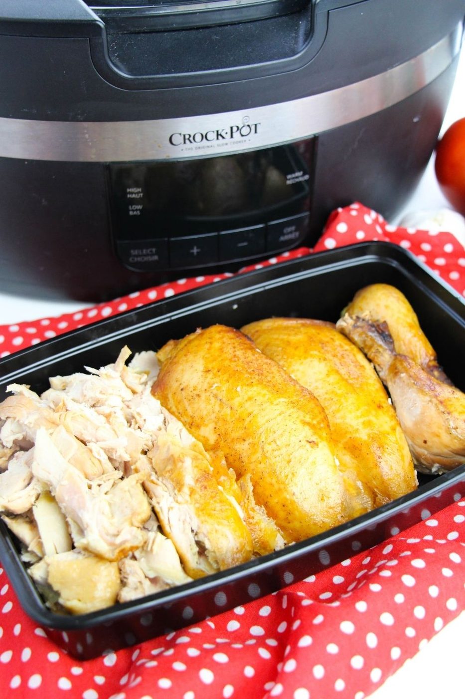 chicken diced up in a black container with crockpot behind it on table