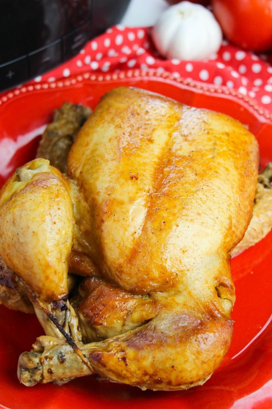 whole chicken on a red plate with veggies behind it