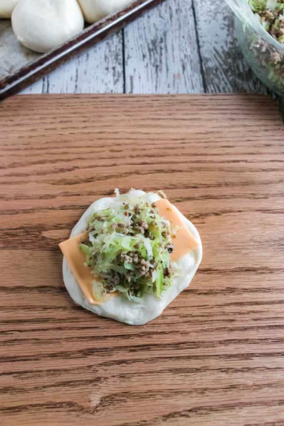 Raw bread dough with a slice of cheese and meet and cabbage filling in the center 