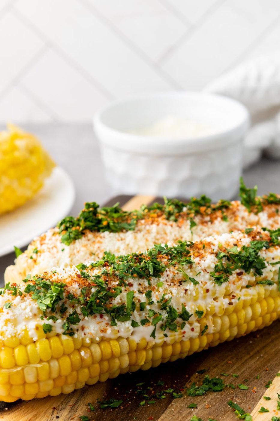 two corn on the cobs on table with sauce and sprinkles 