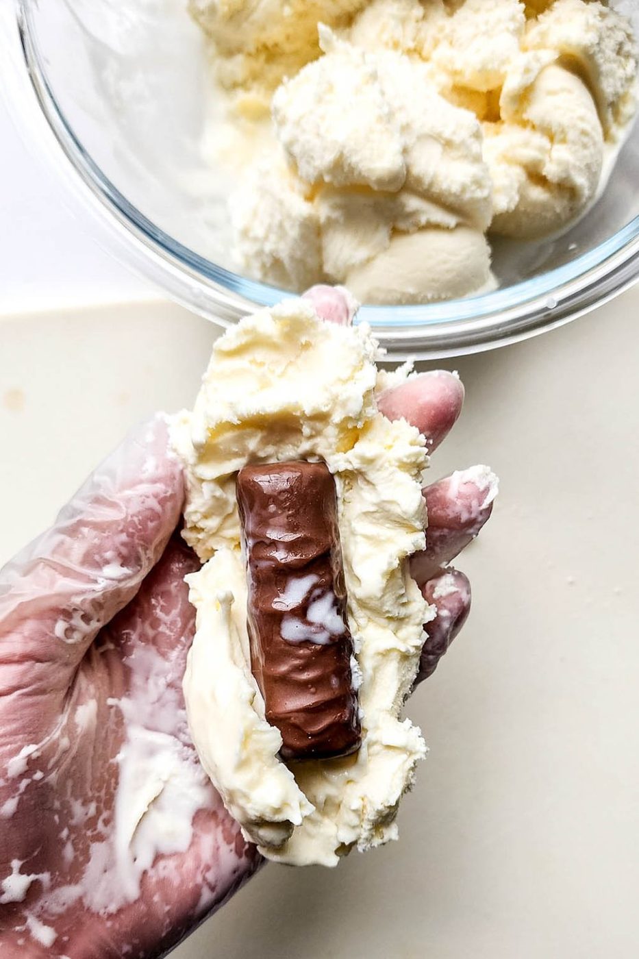 ice cream being pressed around Twix candy bar in hand with a glove on 