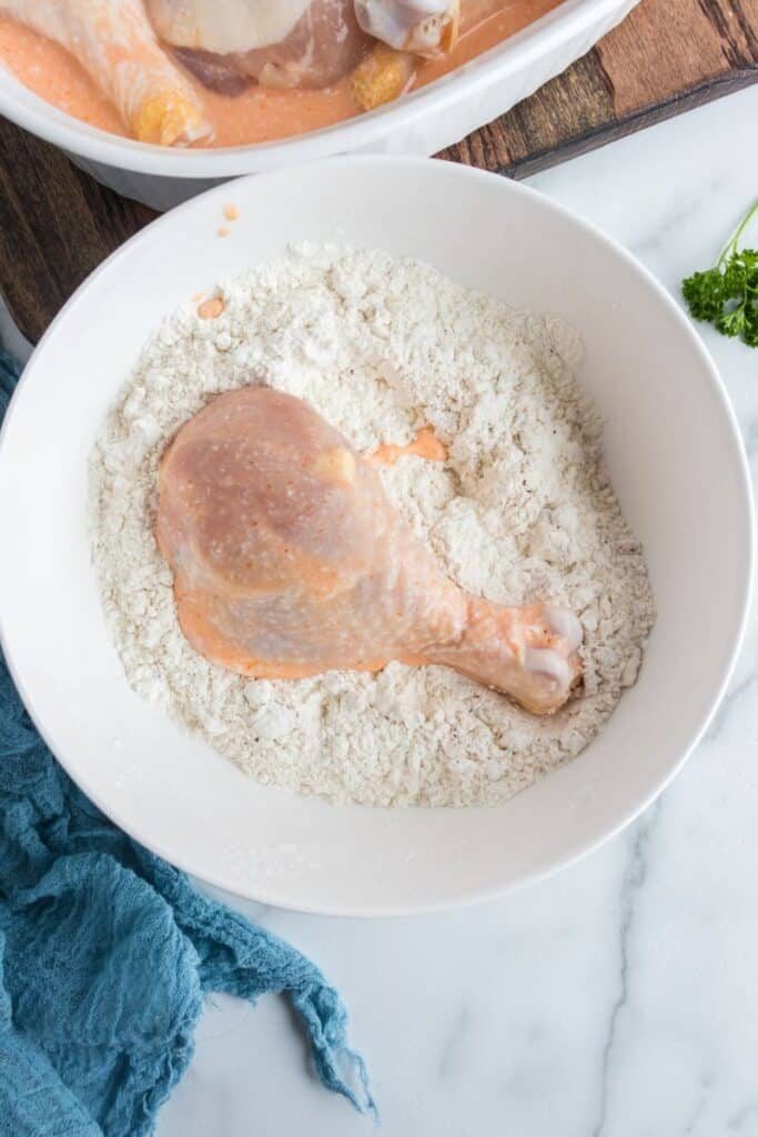 raw chicken leg in a flour mixture sitting on table 