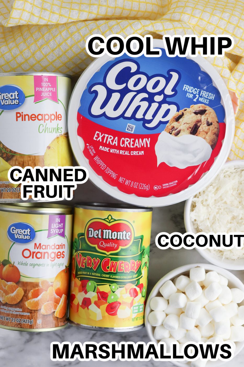 canned fruit, tub of Cool whip, and coconut and marshmallows in bowls on table 