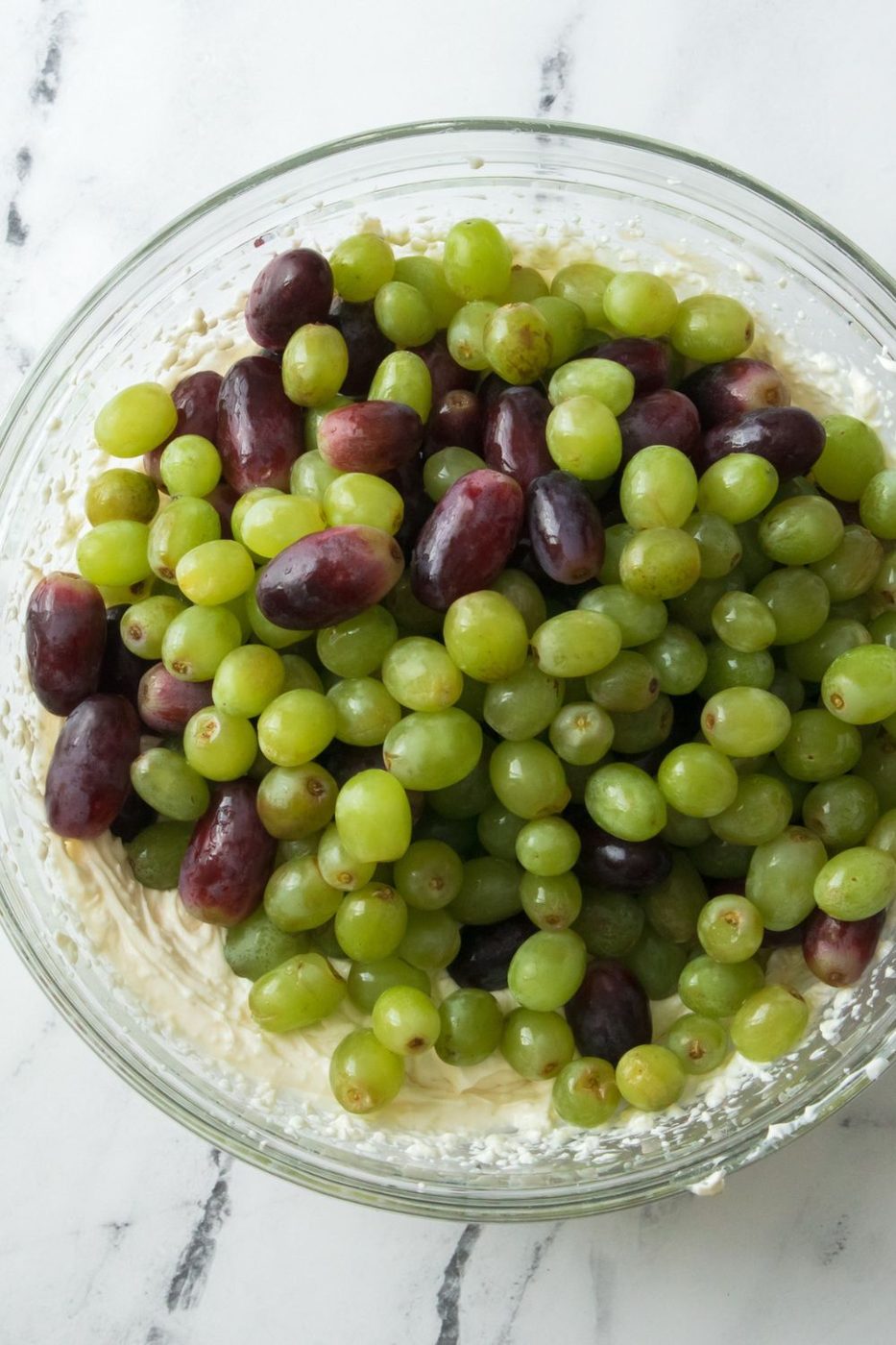 red and green grapes on top of a dressing in a glass bowl