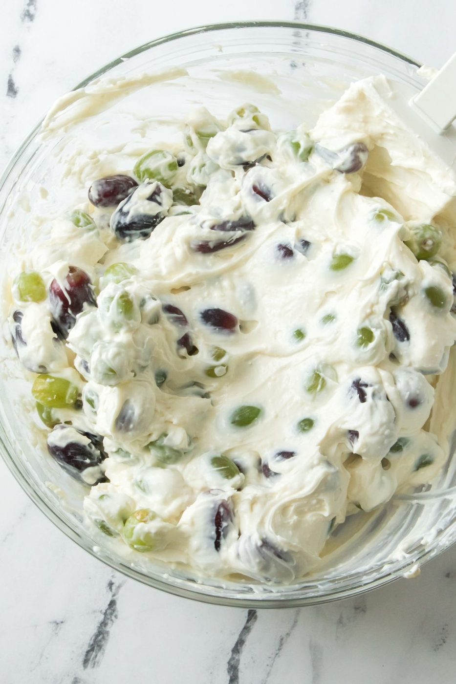 creamy grape salad folded together in a glass bowl on table 