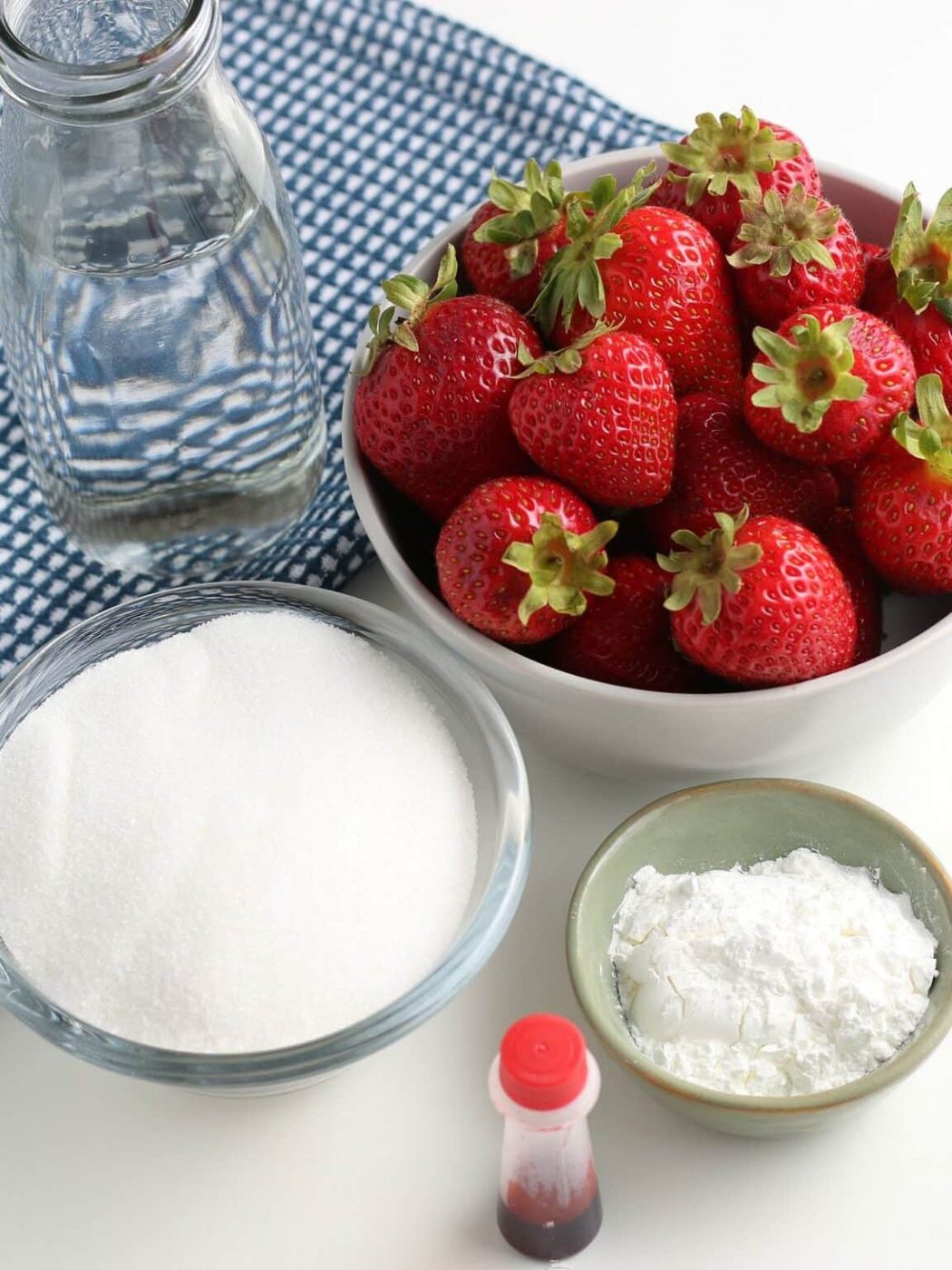 Easy strawberry sauce ingredients in bowls on the table with a blue table to the side 