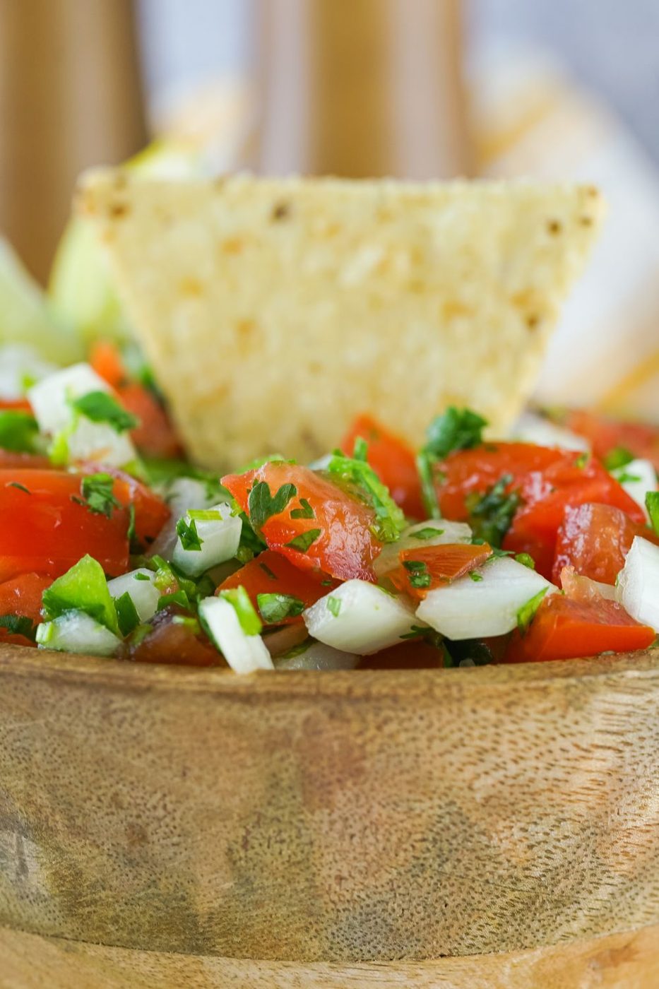 wooden bowl with pico de gallo in it with a chip sticking out the top