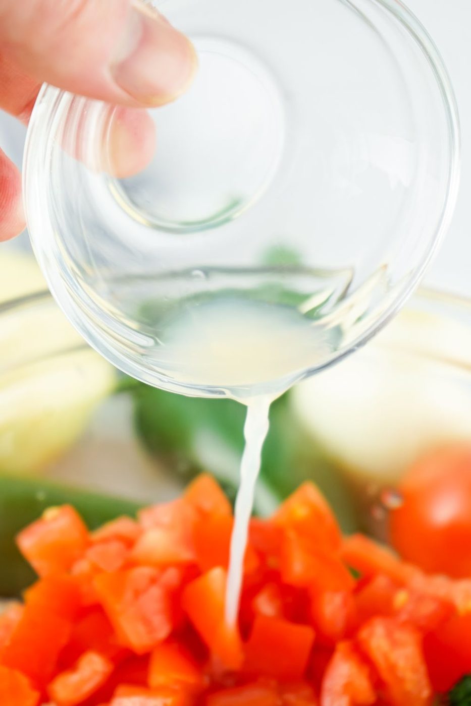 lime juice being poured into a bowl with tomatoes and onions in it