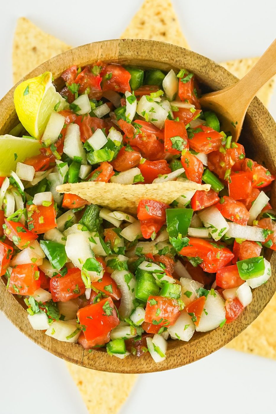 pico de gallo in a wooden bowl with tortilla chips around the bowl on table