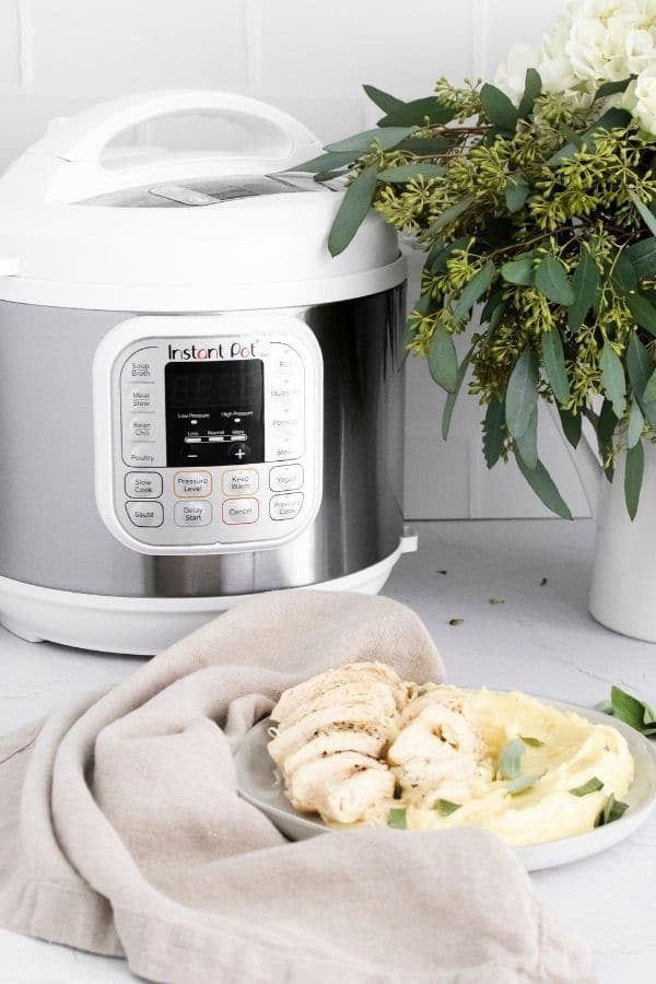 potatoes and chicken in a plate with instant pot and flowers to the back of it 