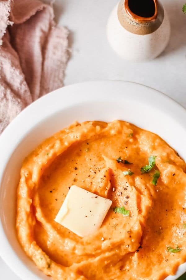 sweet potatoes mashed in a bowl with slab of butter on top