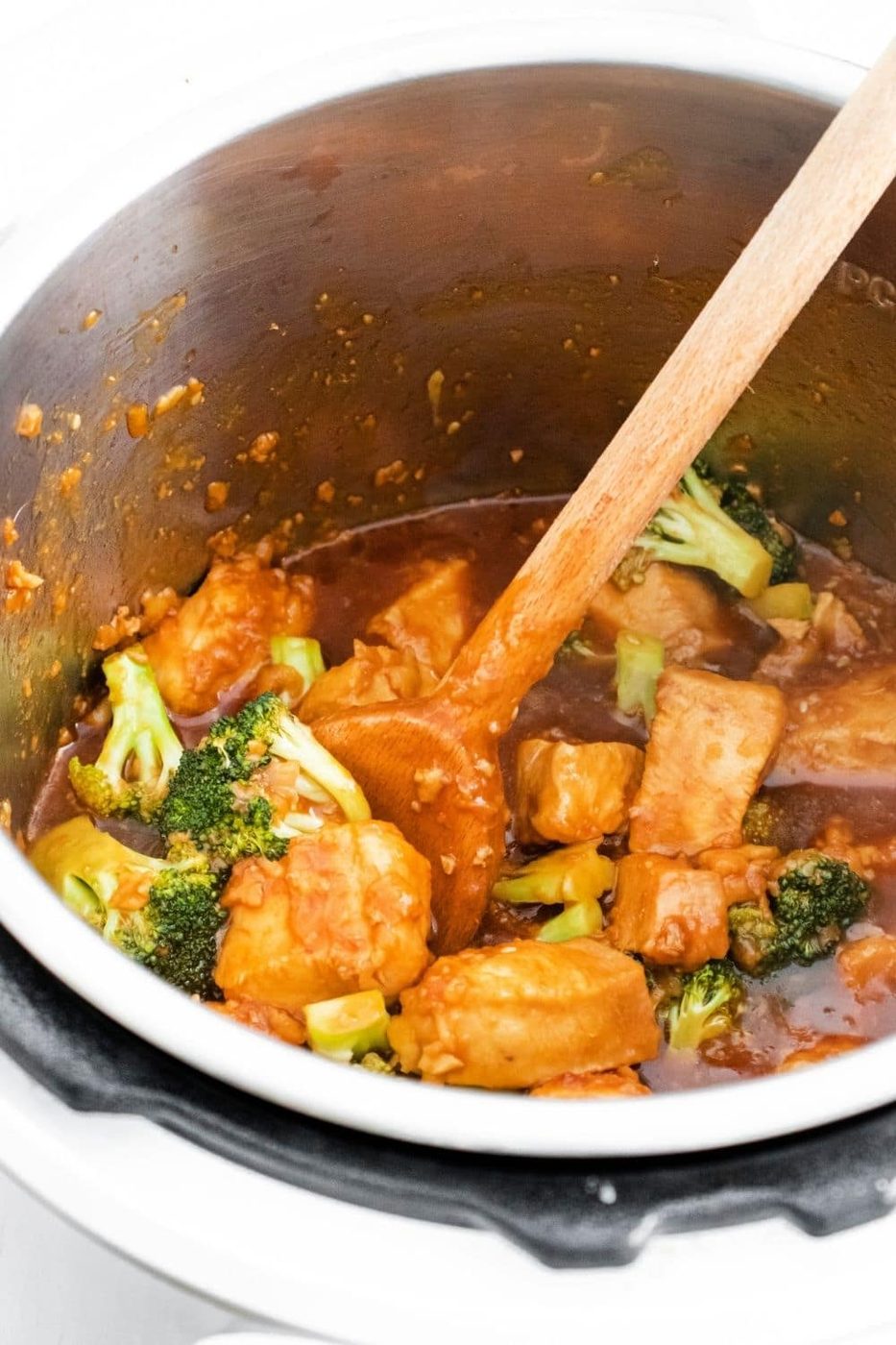 instant pot with sesame chicken and broccoli with wooden spoon