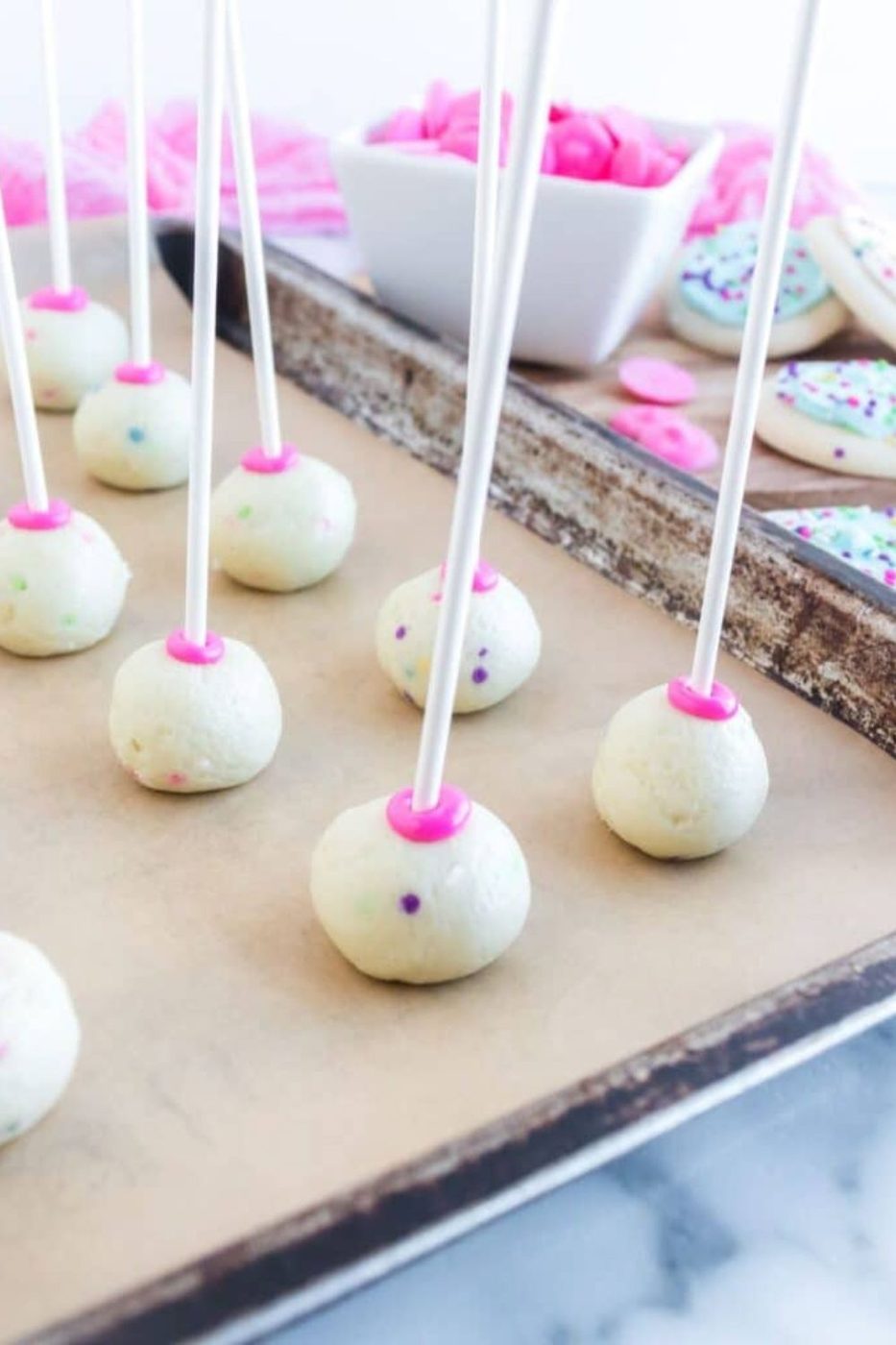 cookie cake pops with sticks in them sitting on a cookie sheet