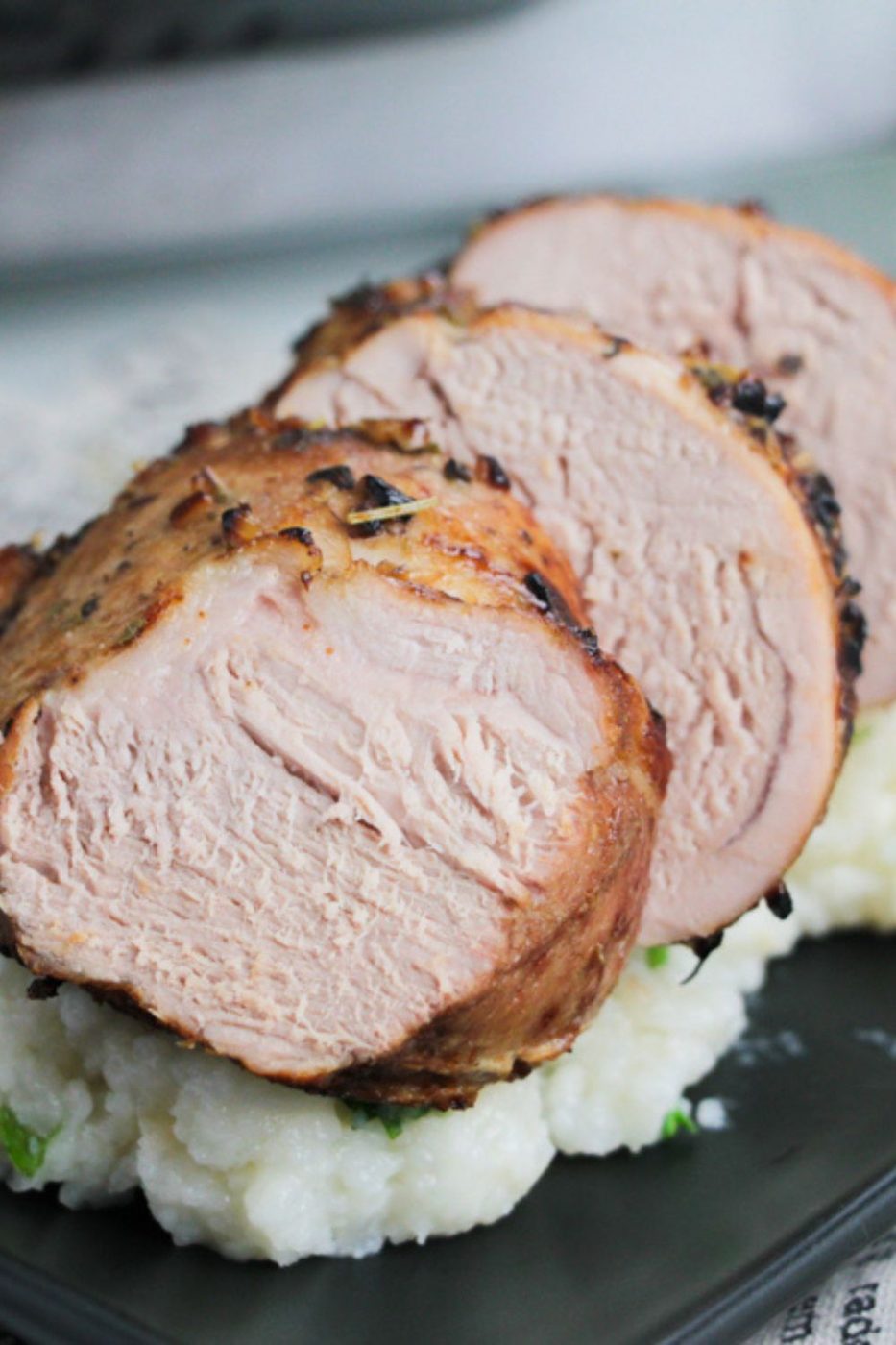 close up look of sliced pork tenderloin with mashed potatoes under it on table 
