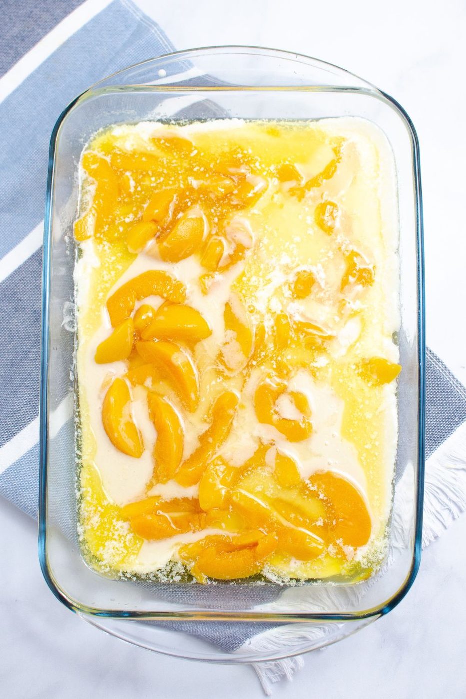 raw peach cobbler batter in a clear glass baking dish sitting on table 