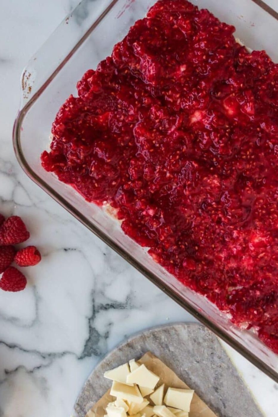 crushed raspberry mixture spread in a glass casserole pan with fresh berries to the side