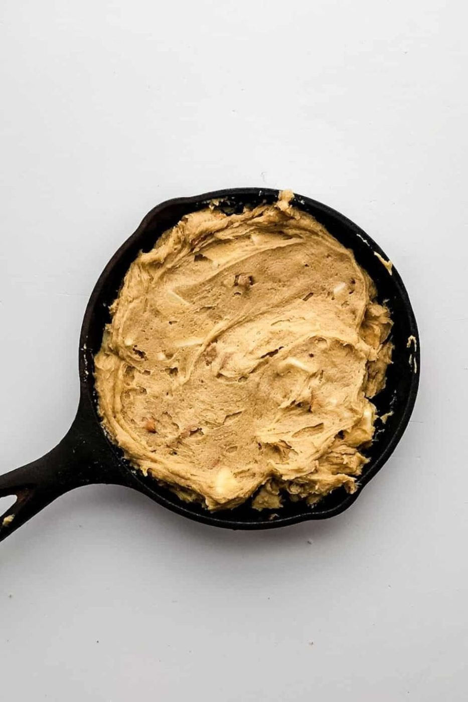 raw cookie dough spread into a cast iron pan on a white table 