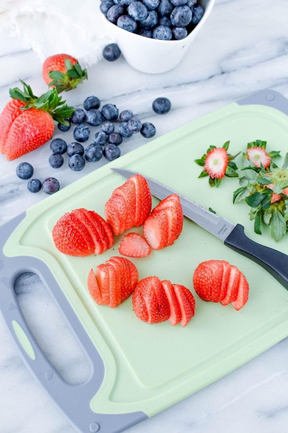 sliced berries on a cutting board and blueberries to side of cutting board on counter 