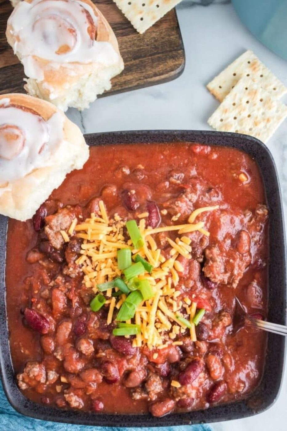 bowl of chili with cinnamon roll and crackers around the bowl 