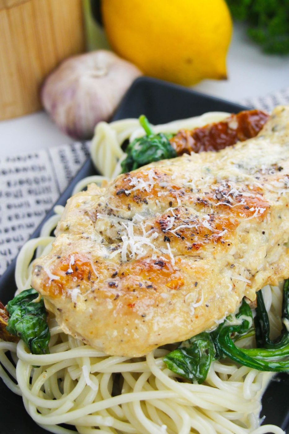 chicken tuscany sitting on top a bed of spaghetti noodles on table 