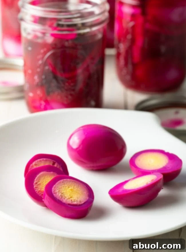 A vibrant pink hard-boiled egg sliced into three perfect rings, artfully arranged on a clean white background alongside another whole egg and a third egg cut neatly in half, highlighting the beautiful color transformation and ready for serving.