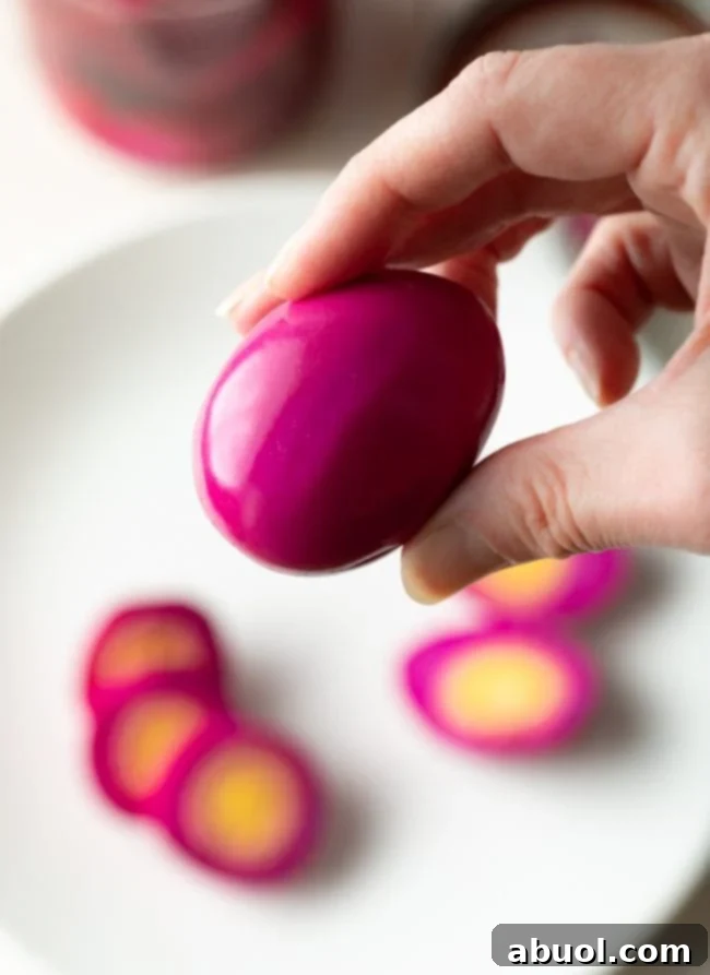 A hand gently holds a vibrant pink beet pickled egg, showcasing its inviting color and smooth texture, ready to be enjoyed.