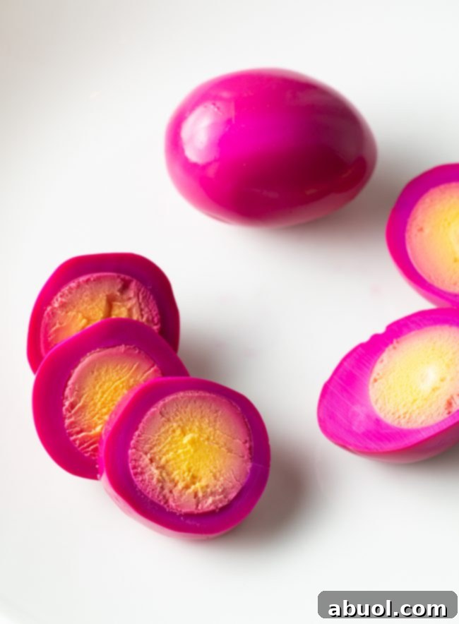 A vibrant pink hard-boiled egg sliced into three perfect rings, artfully arranged on a clean white background alongside another whole egg and a third egg cut neatly in half, highlighting the beautiful color transformation.