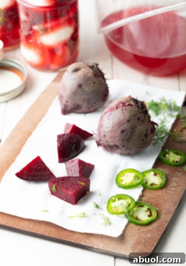 Chunks of raw beets, thinly sliced jalapenos, and two whole fresh beets are neatly arranged on a wooden cutting board, prepped for pickling.