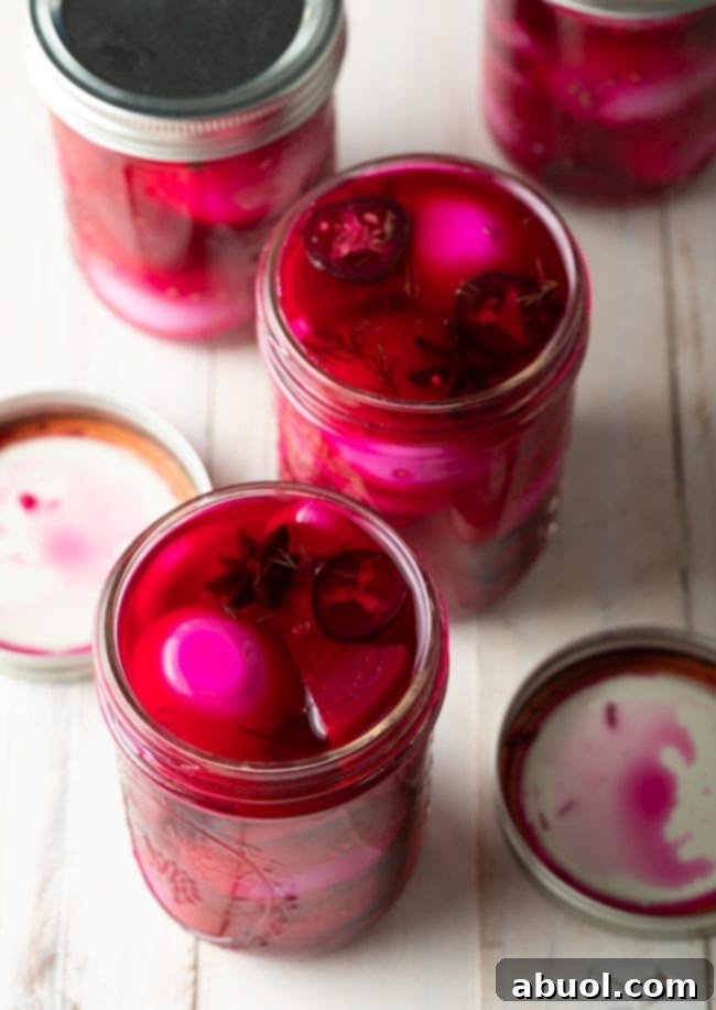 A close-up shot of the finished spicy beet pickled eggs in a glass jar, demonstrating their rich pink color and the fresh ingredients suspended in the brine.