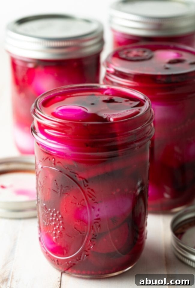 A close-up view of a single pint jar, beautifully filled with vibrant pink spicy pickled eggs, interspersed with tender chunks of beets, crisp slices of jalapeno, and aromatic whole star anise, showcasing the appetizing contents.