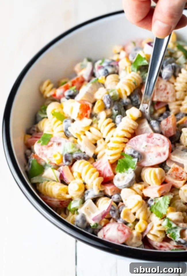 A hand holding a spoon and scooping southwest pasta salad out of the salad bowl, ready to be enjoyed.