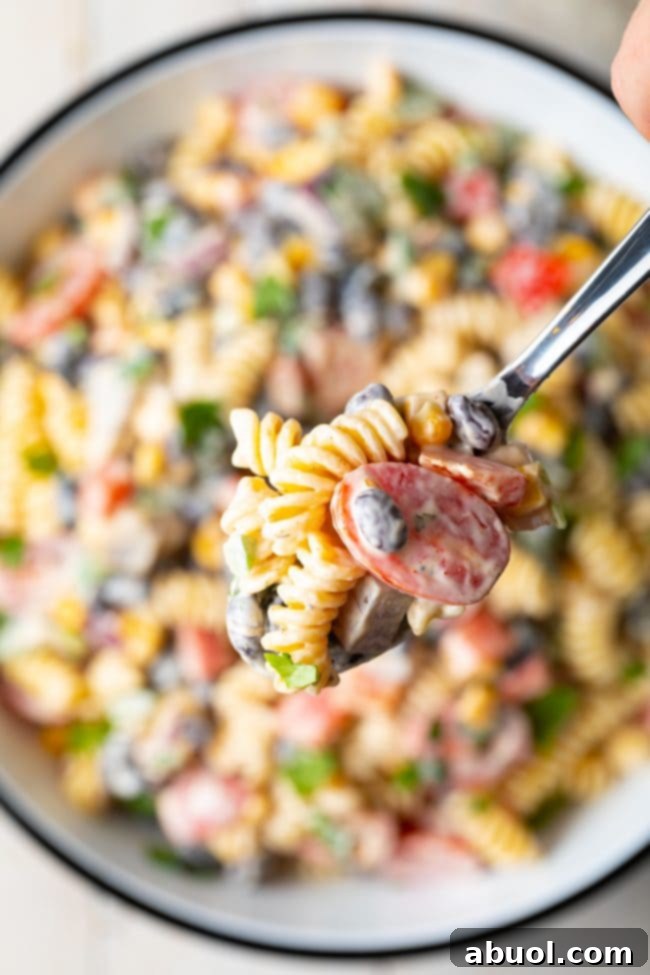 A hand holding a spoon with a scoop of creamy Southwest pasta salad over the pasta bowl, ready to serve.