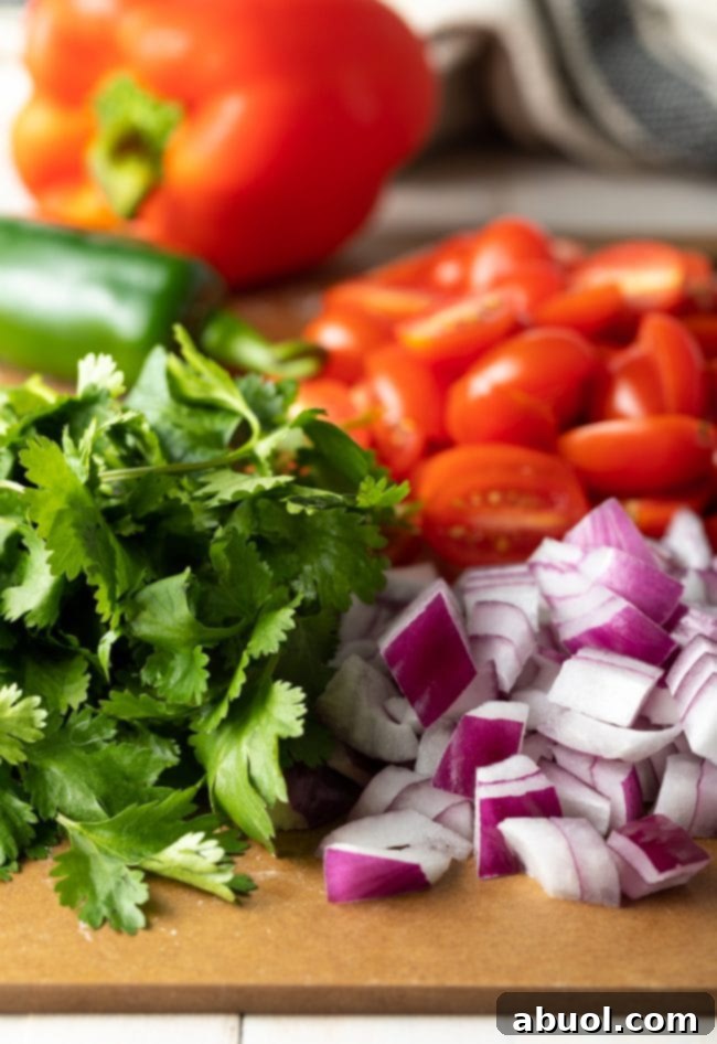Chopped cilantro, onion, tomatoes, and peppers on a cutting board, ready for the pasta salad.