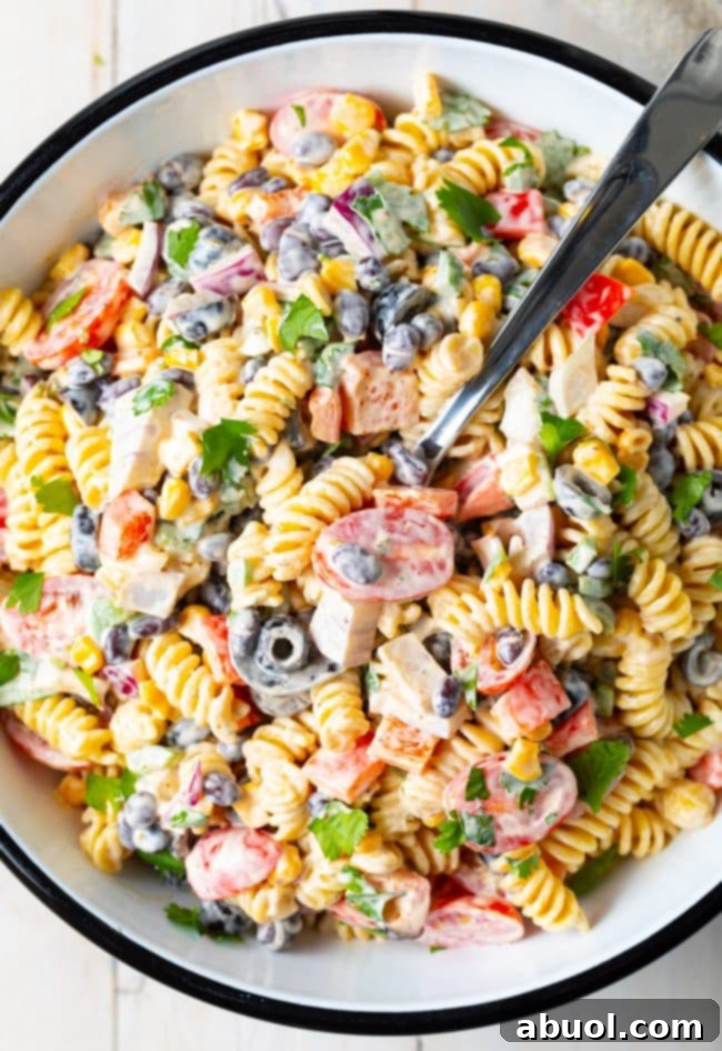 Pasta salad with creamy ranch dressing, veggies, cilantro, and black beans in a salad bowl with a serving spoon.