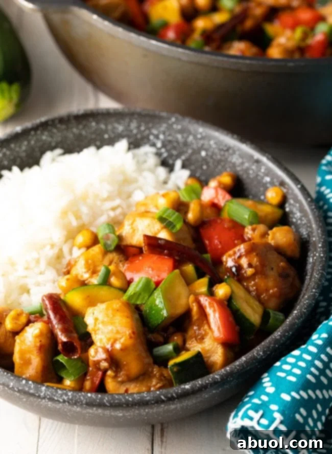 A black bowl filled with steaming white rice and a generous serving of our irresistible homemade Kung Pao Chicken, garnished with fresh green onions and peanuts.