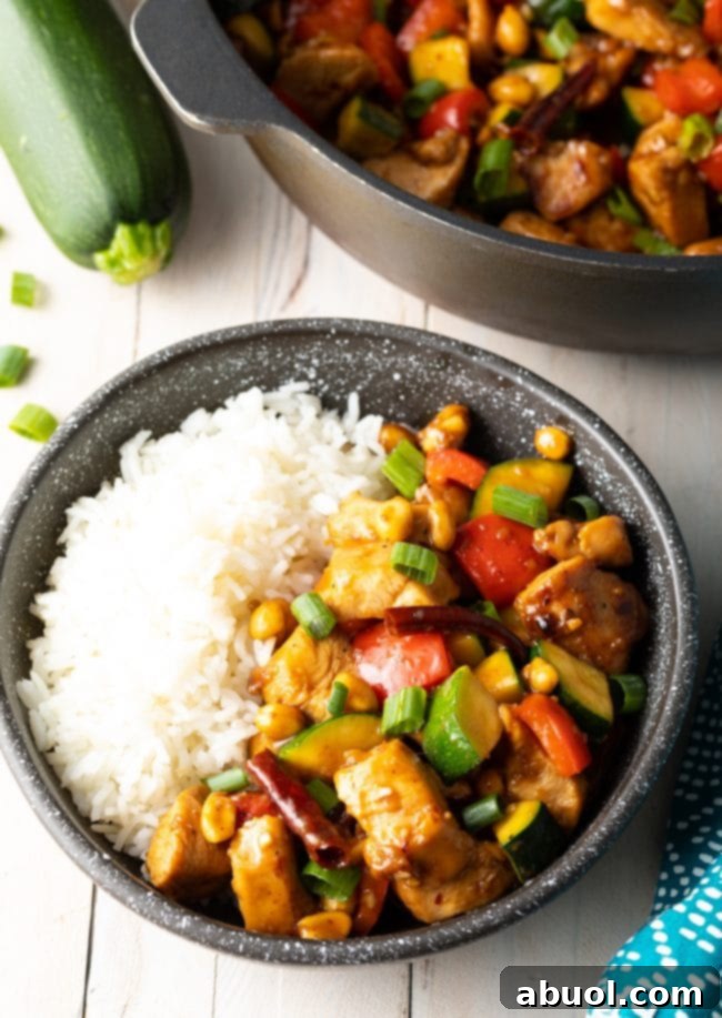 An inviting black bowl filled with authentic Kung Pao Chicken and fluffy steamed white rice, garnished with green onions and ready to be enjoyed.