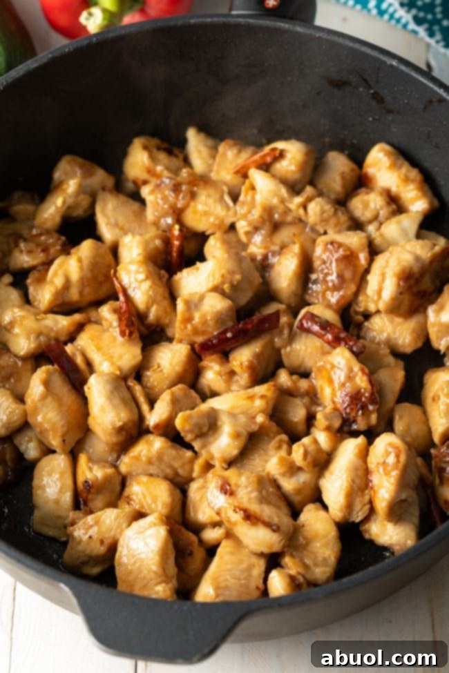 Chopped chicken and fiery red chiles sizzling in a cast iron skillet during stir-frying.