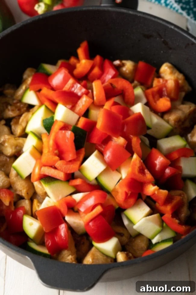 Vibrant chopped zucchini and red bell peppers added to a cast iron skillet, ready to be stir-fried.